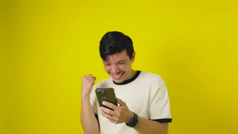 Cheerful young man looking at his cell phone with a celebratory gesture on .. Stock Footage 311537653