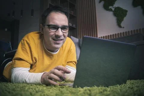 Cheerful young man lying on floor with laptop. side view of young man layin.. Stock Photos