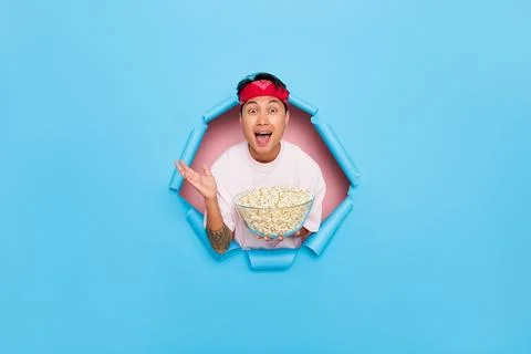 Cheerful young man posing inside cutout on blue background, holding a bowl full Stock Photos