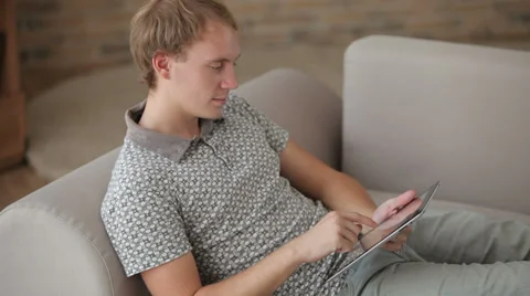 Cheerful young man relaxing on sofa using touchpad looking at camer and smiling Video stock 34278209