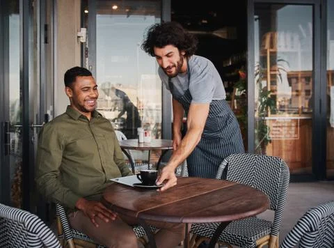 Cheerful young man serving afro-american customer at coffee shop Stock Photos