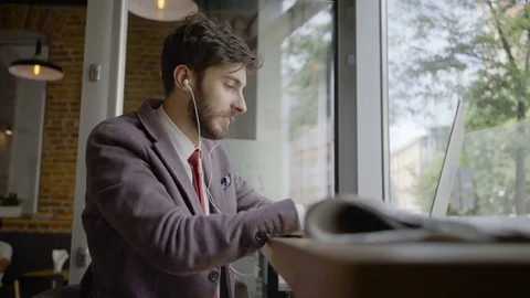 Cheerful young man sitting in a cafe and working on laptop while listening to Stock Footage 79797029