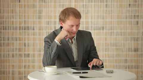 Cheerful young man sitting at table using touchpad and smiling at camera Stock Footage 34278224