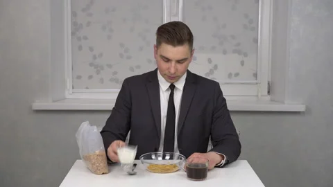 A cheerful young man in a suit eats cereal and drinks coffee. Young businessman Stock Footage 150273967