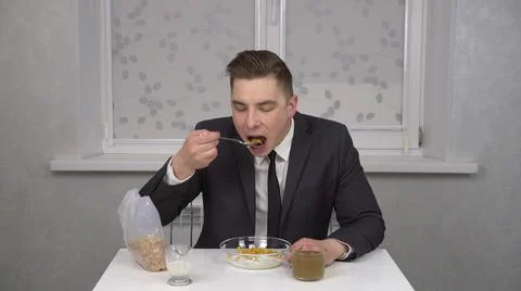 A cheerful young man in a suit eats cereal and drinks coffee. Young businessman Stock Photos