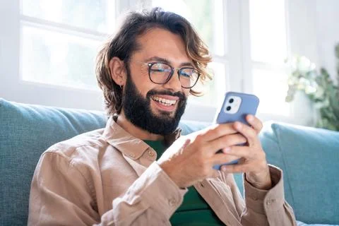 Cheerful young man texting using smartphone at home chatting, social media Stock Photos