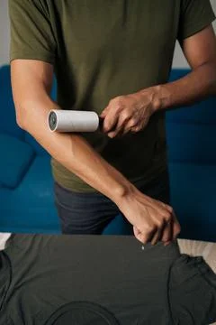 Cheerful young man using sticky lint roller to efficiently remove hair and fluff Stock Photos