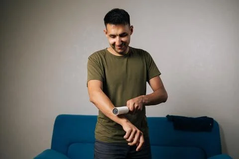 Cheerful young man using sticky lint roller to efficiently remove hair and fluff Stock Photos