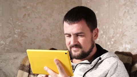 Cheerful young man is using a tablet computer on couch at home. Stock Footage 83584900