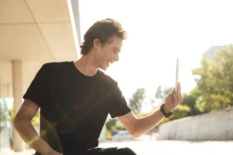 Cheerful young man using tablet for video chat at university campus on sunny day Stock Photos
