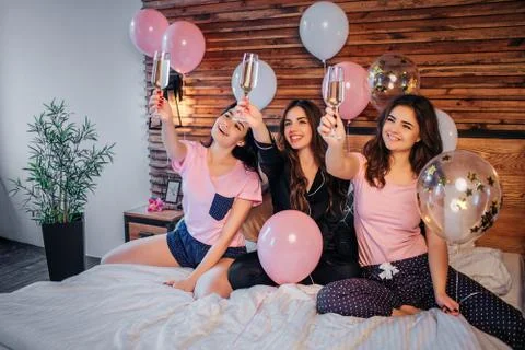 Cheerful young models sit on bed in festive room. They hold glasses with Stock-Fotos