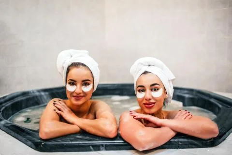Cheerful young models sit in jacuzzi. It is full of water and foam. Young women Stock Photos