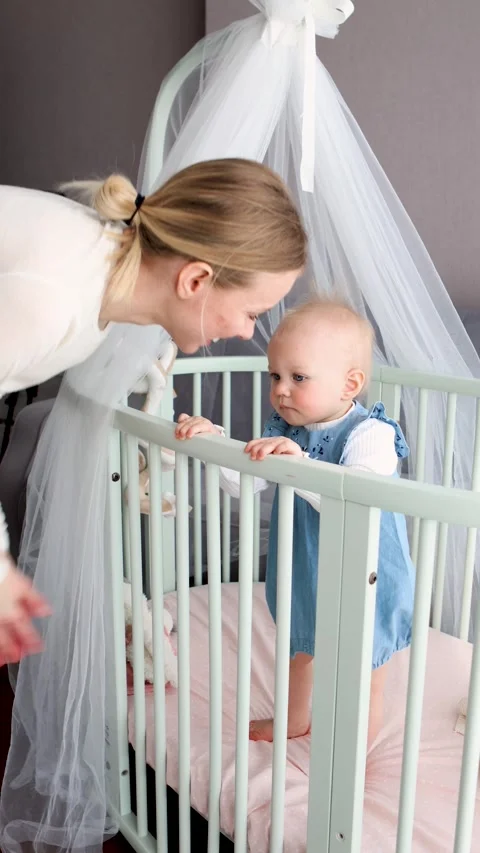 Cheerful young mom dancing and playing with smiling baby daughter in crib at Stock Footage 317008055
