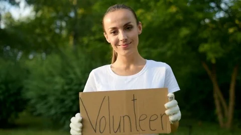 Cheerful young woman holding paper placard with volunteer inscription Stock Footage