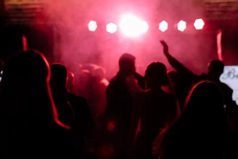 Cheering crowd in front of bright red stage lights. Silhouette image of peopl Stock Photos