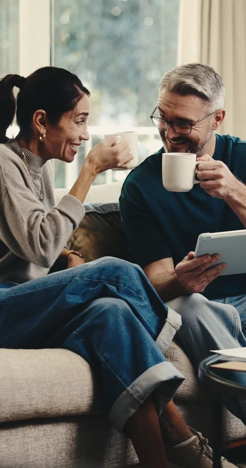 Cheers, coffee and tablet with couple on sofa for booking success, bonding and Stock Footage 342327447