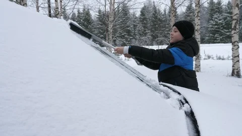 Cheery boy cleaning a car windshield with a long broom in a snowy forest in Stock-Footage 123088731