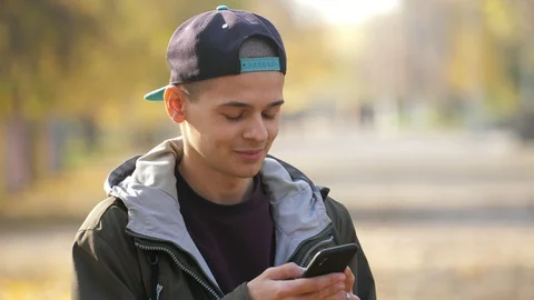 Cheery young guy standing in a park and browsing the net in autumn in slow Stock-Footage 120009893