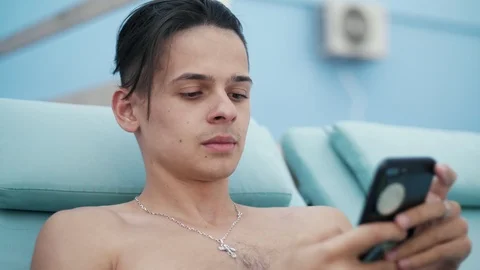 Cheery young man lying on a sunbed and browsing the net on her phone in summer Stock-Footage 116504618