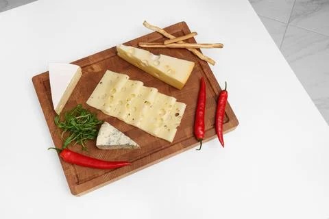 Cheese board on a white table. Different types of cheese, chili, microgreens. Stock Photos