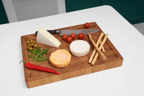 Cheese board on a white table. Different types of cheese, tomatoes, chili. Stock Photos