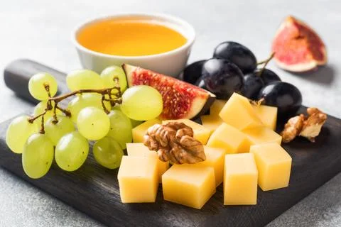 Cheese cubes, fresh fruit figs grapes Honey walnut on wooden chopping Board.. Stock Photos