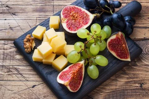 Cheese cubes, fresh fruit figs grapes Honey walnut on wooden chopping Board.. Stock Photos
