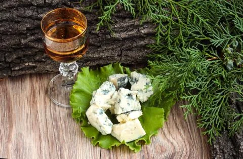 Cheese cubes on a lettuce leaf with a stack of cognac on the background of tr 스톡 사진