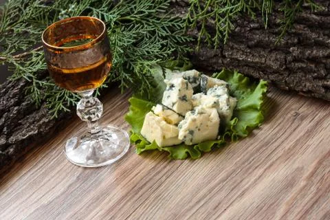 Cheese cubes on a lettuce leaf with a stack of cognac on the background of tr Stock Photos