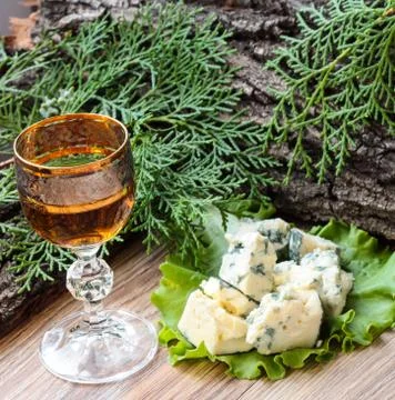 Cheese cubes on a lettuce leaf with a stack of cognac on the background of tr 스톡 사진