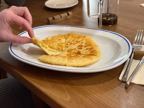 Cheese filled flatbread sliced on white plate in cafe. Traditional pastry, ca Stock Photos