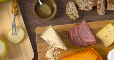 Cheese, ham and pears over wooden boards beside sliced bread, honey and wine  Stock Footage 194450005