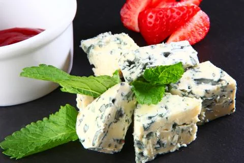 Cheese with a noble blue mold on a black plate with strawberries Stock Photos