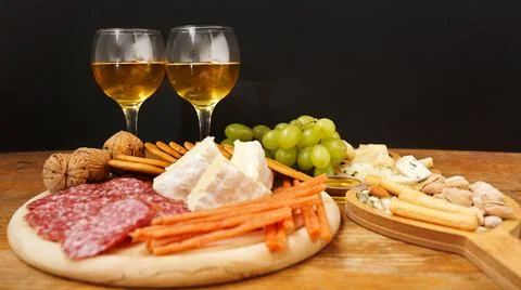 Cheese platter with assorted cheeses, grapes, nuts over black background Stock Photos