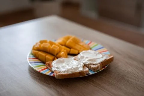 Cheese spread toasts with mango cut in cubes on a colorful plate on a wooden  Stock Photos