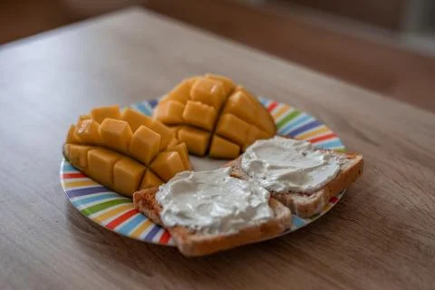 Cheese spread toasts with mango cut in cubes on a colorful plate on a wooden  Stock Photos