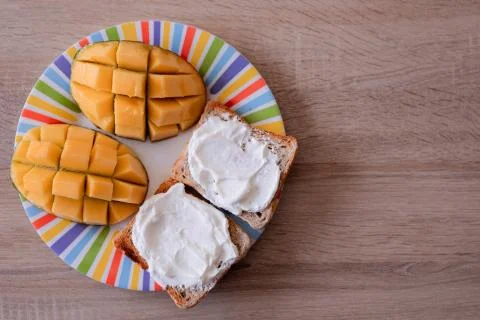 Cheese spread toasts with mango cut in cubes on a colorful plate on a wooden  Stock Photos