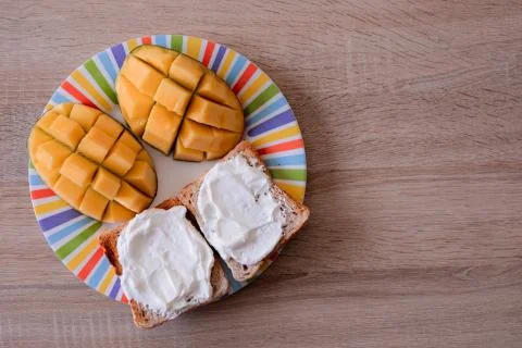 Cheese spread toasts with mango cut in cubes on a colorful plate on a wooden  Stock Photos