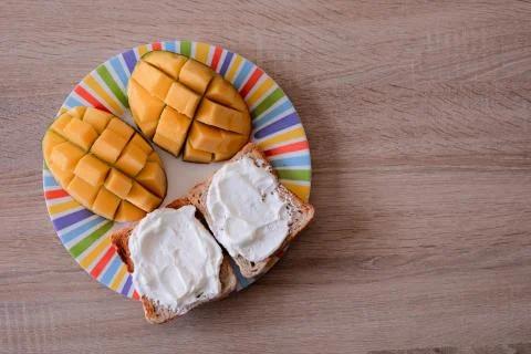 Cheese spread toasts with mango cut in cubes on a colorful plate on a wooden  Stock Photos