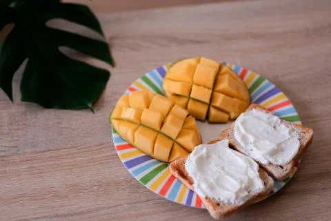 Cheese spread toasts with mango cut in cubes on a colorful plate on a wooden  Stock Photos