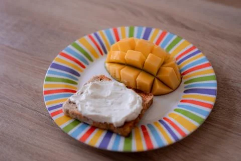 Cheese spread toasts with mango cut in cubes on a colorful plate on a wooden  Stock Photos