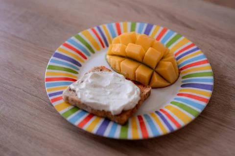 Cheese spread toasts with mango cut in cubes on a colorful plate on a wooden  Stock Photos