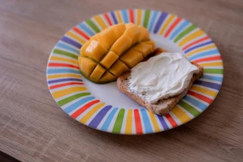 Cheese spread toasts with mango cut in cubes on a colorful plate on a wooden  Stock Photos