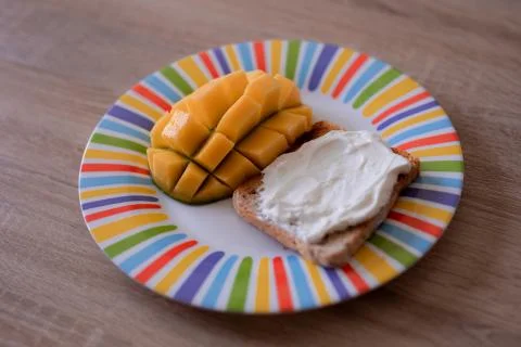 Cheese spread toasts with mango cut in cubes on a colorful plate on a wooden  Stock Photos