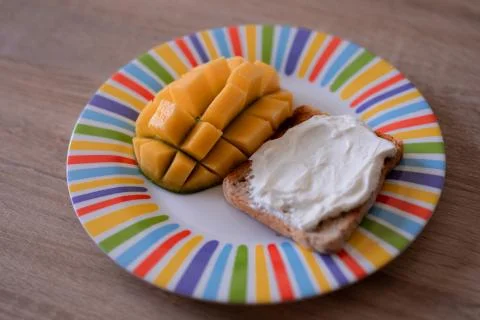 Cheese spread toasts with mango cut in cubes on a colorful plate on a wooden  Stock Photos