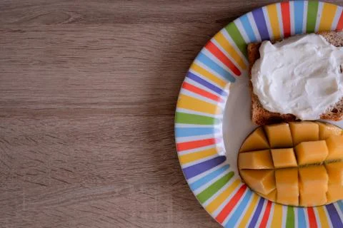 Cheese spread toasts with mango cut in cubes on a colorful plate on a wooden  Stock Photos