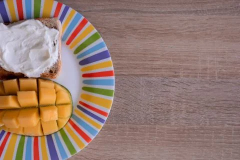 Cheese spread toasts with mango cut in cubes on a colorful plate on a wooden  Stock Photos