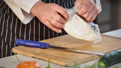 Cheese wrapped in plastic wrap. Microplastics in food. Chef unpacking cheese. Vídeo Stock 301081380