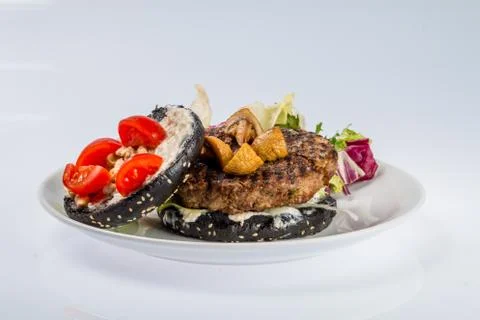 Cheeseburger with black bread, beef cutlet, bacon, tomatoes and cheese slices Stock Photos