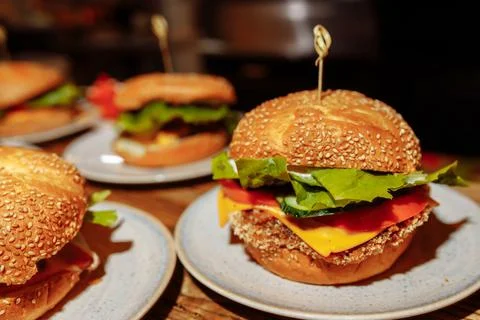 Cheeseburgers and fries on table top with onion, tomato, lettuce and cheese Stock Photos